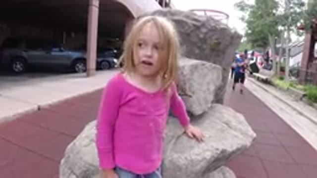 WINTER PARK COLORADO-2019: A Blond Child Sits On Artificial Rocks Near A Parking