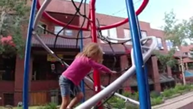 WINTER PARK COLORADO-2019: A Child In A Pink Shirt And Blue Jean Shorts Plays On Jungle Gym