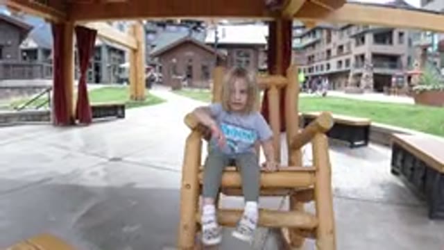WINTER PARK COLORADO-2019: Child Playing in Rocking Chair in Square with Buildings and People Passing By