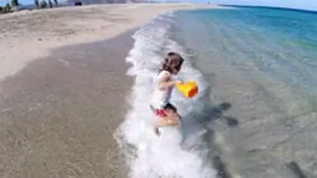 LOS CABOS MEXICO-2019: A Little Girl Holding A Yellow Toy Skips A Low Wave On A