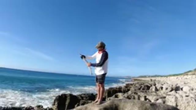 LOS CABOS MEXICO-2019: A Man Standing On The Rocks Next To The Sea Is Holding A Fishing Rod
