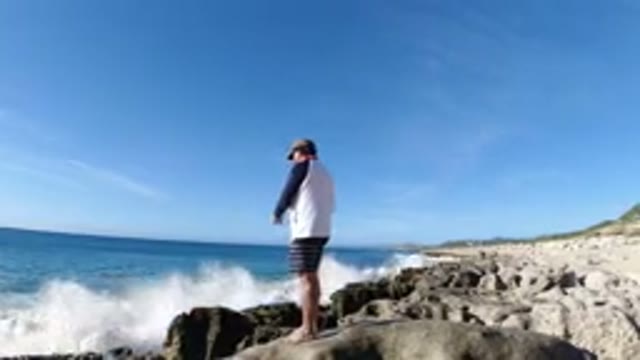 LOS CABOS MEXICO-2019: A Man Standing On A Rock Throwing A Large Fish Back
