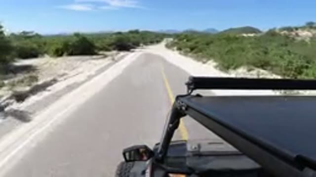 LOS CABOS MEXICO-2019: Vehicle Moves Down Two Lane Road Partially Covered By Sand and Shrubs