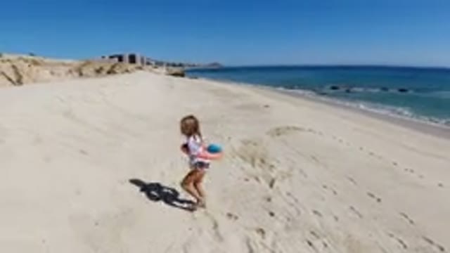 LOS CABOS MEXICO-2019: Little Girl With Orange Floating Toy Walking On Sandy Beach