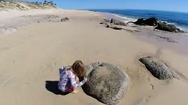 LOS CABOS MEXICO-2019: Blonde Child On Beach Playing In Sand Beside Rocks On A Sunny Day