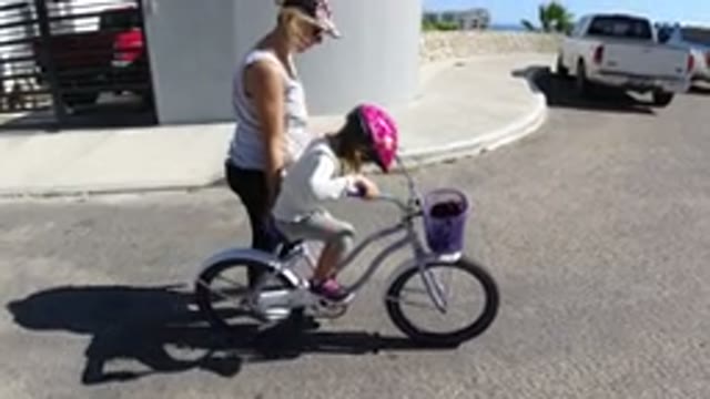 SAN JOSE DEL CABO MEXICO-2020: Girl Learning to Ride Bicycle with Mother Helping