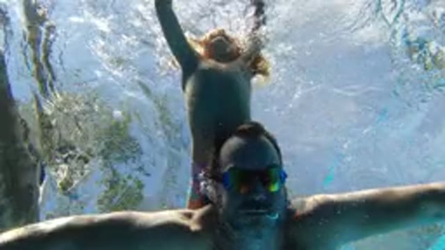 LOS CABOS MEXICO-2020: A Child Hangs Onto The Back Of A Man Swimming Underwater