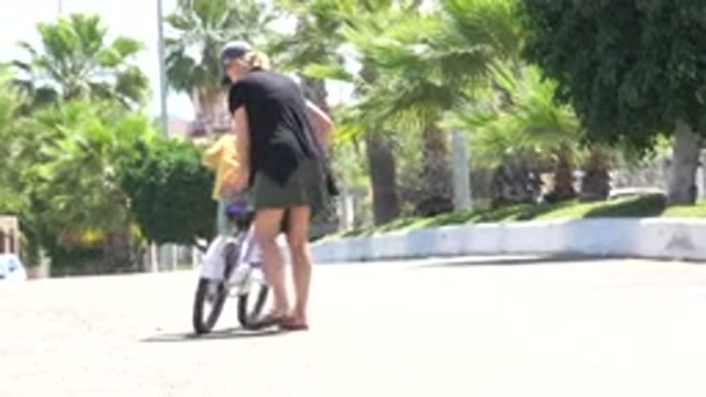 LOS CABOS MEXICO-2020: A Woman Teaching A Child To Ride A Bike In A Park On A