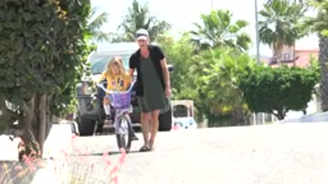 LOS CABOS MEXICO-2020: Woman Helping Girl With Yellow Shirt Ride Bike On Street