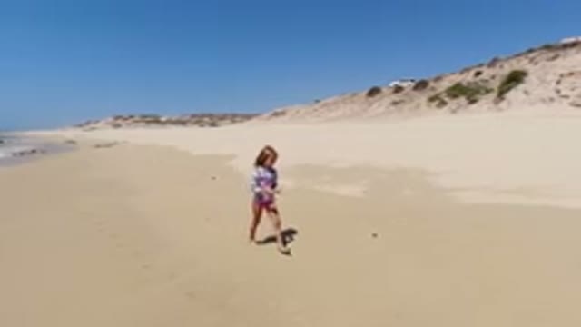LOS CABOS MEXICO-2020: Little Girl Walks Along The Beach Carrying Something In