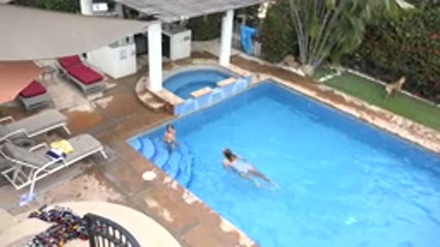 LOS CABOS MEXICO-2020: Woman Swims In Pool Towards Child On Stair While Dog Lays