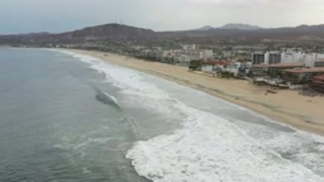 LOS CABOS MEXICO-2020: Waves On Beach In Front Of Buildings With Hills In
