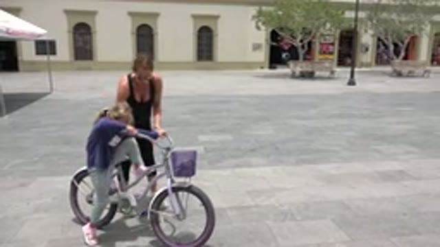 LOS CABOS MEXICO-2020: Adult Woman Helping Young Child Ride Purple Bicycle In