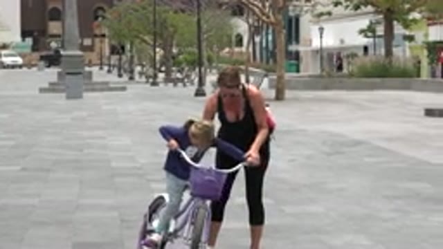 LOS CABOS MEXICO-2020: A Lady Helping A Small Girl To Ride A Purple Colored Bicycle