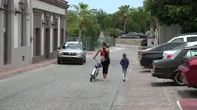 LOS CABOS MEXICO-2020: Woman Walking A Bicycle With A Small Child Along A Cobblestone Street