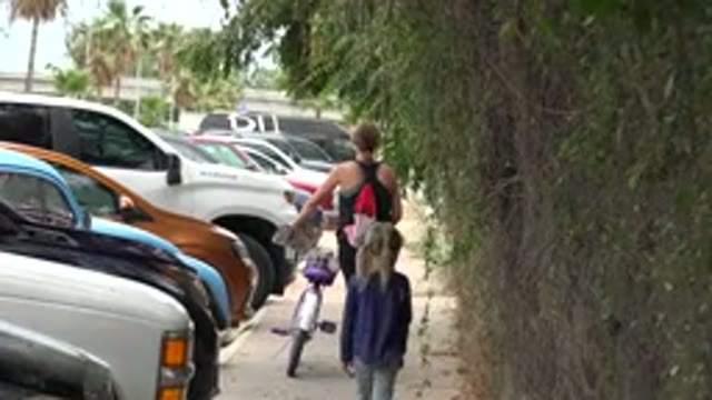 LOS CABOS MEXICO-2020: Mother And Child Walk On A Sidewalk With Cars Crowded To