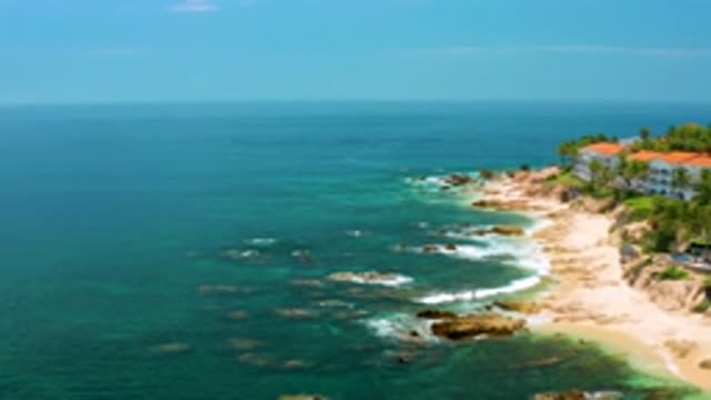 PALMILLA BEACH BCS MEXICO-2020: Rocky Coastline With Waves; Trees And Red Roofed Buildings