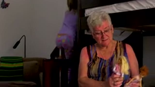 Senior Woman Playing With Dolls On Bed